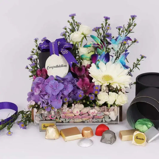 Congratulations flower arrangement with purple hydrangeas, blue orchids, white roses, and chocolates.