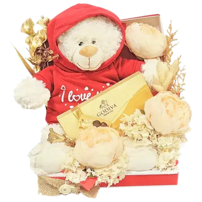 a romantic gift set featuring a box of Godiva chocolates, a soft teddy bear with an "I Love You" hoodie, and a beautiful arrangement of artificial gold flowers, cream peonies, and dried florals