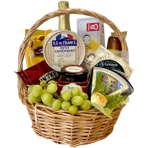 A photo of a wicker gift basket overflowing with a variety of cheeses, grapes, nuts, crackers, a jar of chutney, a bottle of sparkling grape juice, and small hazelnut snacks.