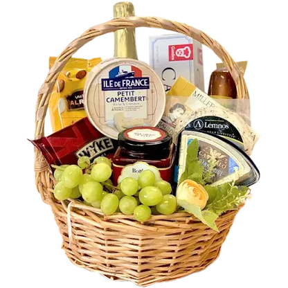 A photo of a wicker gift basket overflowing with a variety of cheeses, grapes, nuts, crackers, a jar of chutney, a bottle of sparkling grape juice, and small hazelnut snacks.