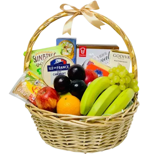 A photo of a wicker gift basket overflowing with colorful fruits, gourmet cheese wedges, a chocolate bar, and various crackers.