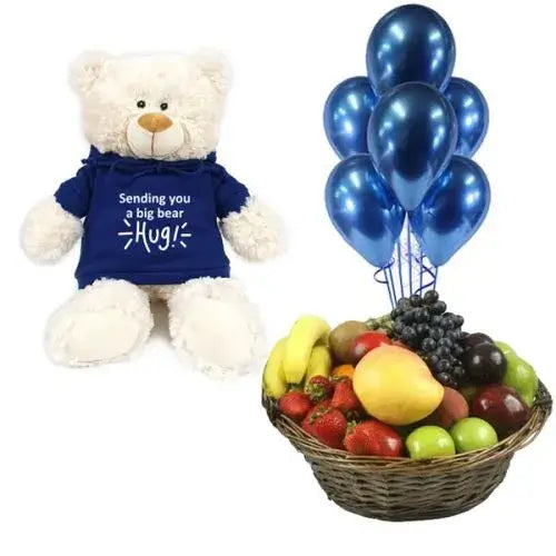 A photo of a large wicker gift basket overflowing with colorful seasonal fruits, a bunch of blue balloons, and a teddy bear holding a heart.