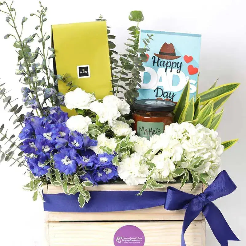 a Father's Day gift hamper with a wooden box overflowing with blue and white flowers, Patchi chocolates, a greeting card, and a scented candle