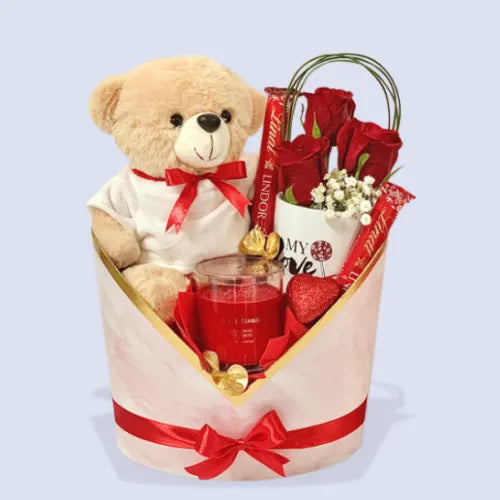 Romantic gift box in Dubai, UAE, featuring a soft teddy, red roses, Lindt Lindor milk chocolates, a mug, scented candle, and greeneries from Giftshop.ae