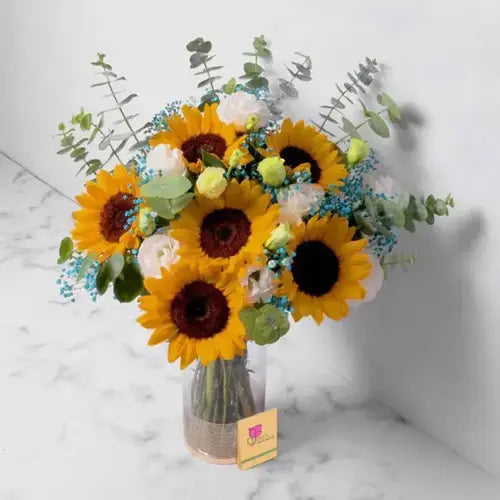 Bright sunflower and rose bouquet in Dubai, featuring fresh sunflowers, white and yellow roses, eucalyptus, and baby breath in a glass vase.